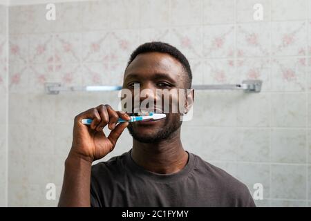 Young black man brushing teeth thoroughly at home. Front view. Looking at camera. Stock Photo