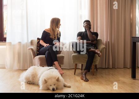 Man and woman arguing seated on living room armchairs with dog sleeping in front. Stock Photo