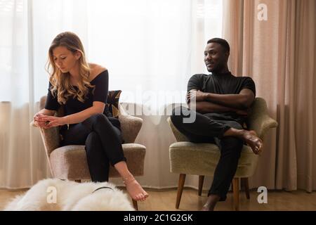 Upset woman looking away from man seated in armchair. Full length. Stock Photo