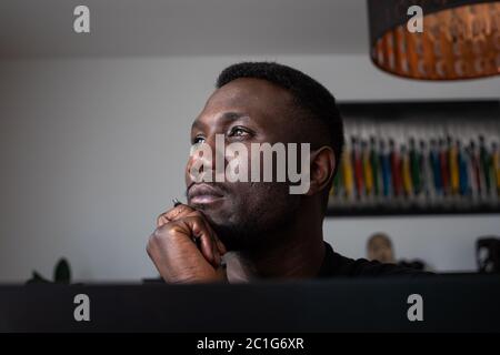 Portrait of black man looking away thinking with hand on chin indoors. Close up. Stock Photo