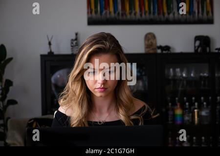 Young blond woman looking downwards at laptop in living room. Medium shot. Stock Photo