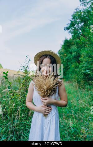 Beautiful girl in a white dress with a bouquet of dried flowers. Young woman in a green park. Girl in a dress and a summer sunny day Stock Photo