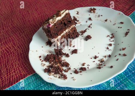The last piece of chocolate sponge cake with cream on a white plate is decorated with multicolored topping with crumbs on a plate on a  tablecloth Stock Photo