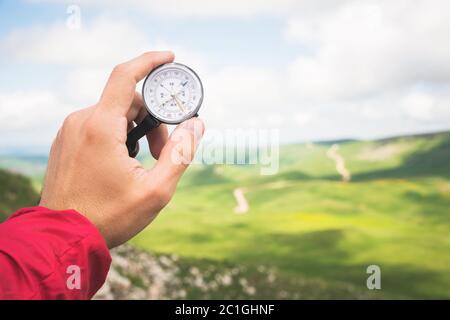 A man's hand of a tourist with an authentic compass on the background of a mountain road landscape Stock Photo