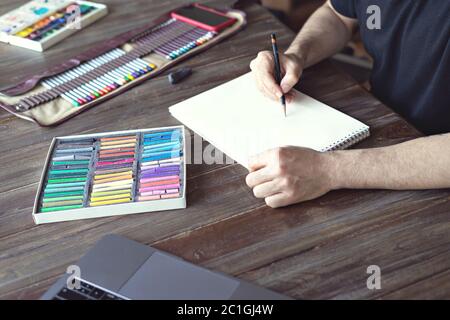 man painting with color pencil and pastel crayon chalks on paper on wooden table Stock Photo