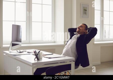 Happy businessman with hands behind head smiling resting runs dreams at a desk in the office. Stock Photo