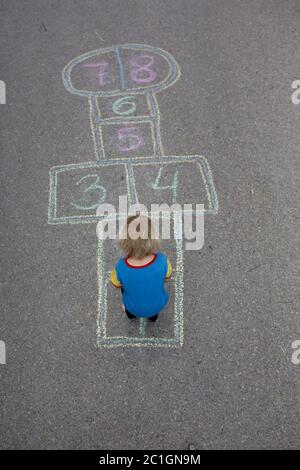 Child, blond boy, playing hopscotch on the street, summertime Stock Photo