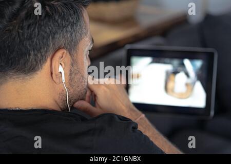 man hand holding using digital tablet watching online cooking master class using headphones. learning cooking remotely Stock Photo