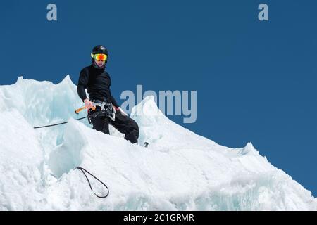 A professional mountaineer in a helmet and ski mask on the insurance does notch the ice ax in the glacier. The work of a profess Stock Photo