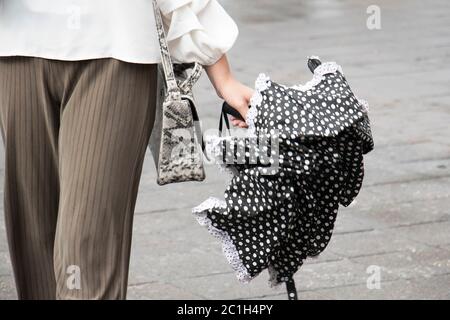 Young woman walking city sidewalk, holding folded umbrella in her hand, from waist down just after rain Stock Photo