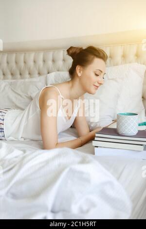 Happy young woomen relaxing on bed and reading book staying at home. Girl learning at home reading literature during quarantine Stock Photo