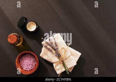 Lavender blossom, sea salt, cream jar, towels and essential oil on black background, top view, flat lay, copy space. Aromatherapy, spa and wellness co Stock Photo