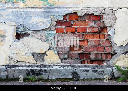 An old wall with peeling beige plaster under which red brickwork is visible Stock Photo