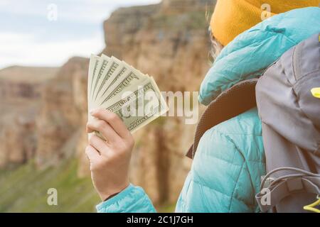 A traveler girl wearing a hat and sunglasses is holding a hundred dollar bills in the hands of a fan against the backdrop of cli Stock Photo