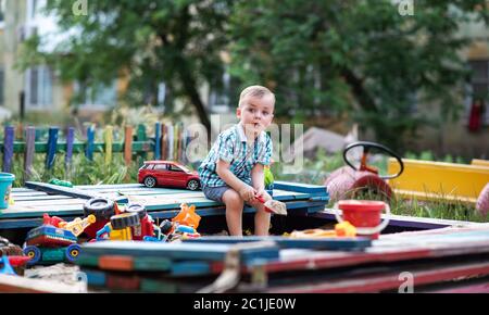 A child plays in the playground with toys in the sandbox. Toddler boy plays in the sand in the summer. Cheerful children's vacation outside. Stock Photo