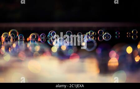shiny iridescent soap bubbles and highlights floating on the water and reflected in the rays of sunlight Stock Photo