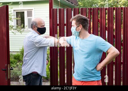 Two men in medical mask greeting each other with elbows on sunny day Stock Photo