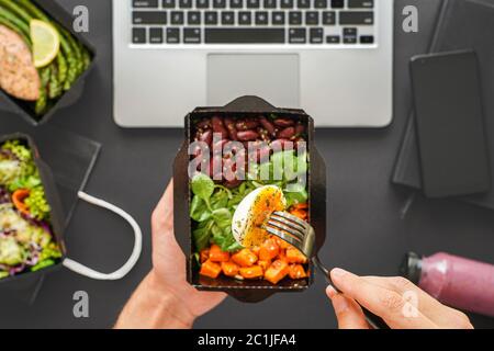 Male hands holding food delivery box eating lunch at work in office, flat lay. Stock Photo