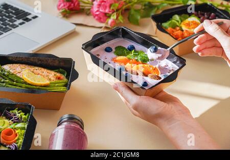 Woman holding lunch delivery box eating working from home office, close up. Stock Photo