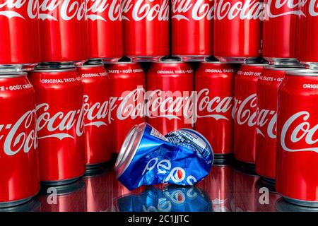 Saint John, NB, Canada - April 28, 2020: Many cans of Coca Cola surround a crushed Pepsi can. Shallow depth of field, focus on Pepsi can. Stock Photo