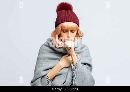 Cute sick young teen woman in red hat, wrapped in warm scarf coughing, closed eyes.Female feeling the first symptoms of illness, isolated.Bronchitis, Stock Photo