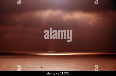 Dramatic skies with sun and sunlit ocean horizon Stock Photo