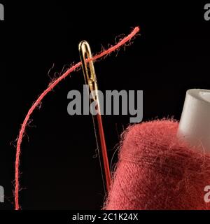 Red thread, threaded into a needle close-up on a black background Stock Photo