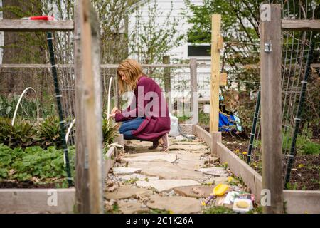 A woman plants seeds in her garden while child plays in background Stock Photo
