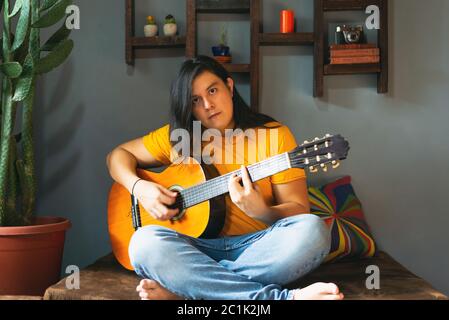 man with long hair playing acoustic guitar at home during quarantine Stock Photo