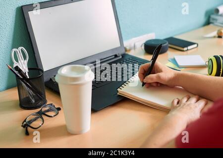Unrecognizable woman writes on her notebook on a desk in her home Stock Photo