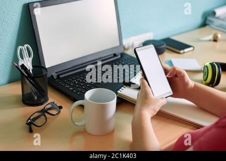 Unrecognizable woman writes on her smartphone at a desk in her home Stock Photo