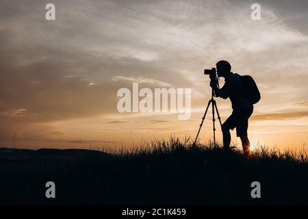 Silhouette of man with tripod taking pictures of sunset Stock Photo