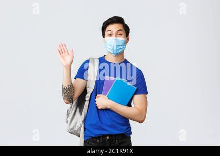 Back to school, studying during covid-19, education and university life concept. Young handsome asian male student, freshman in college waving hand in Stock Photo