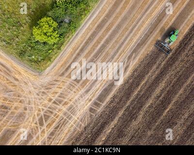 An agricultural field after harvesting with tractor plowing the soil on a summer day. Top view Stock Photo