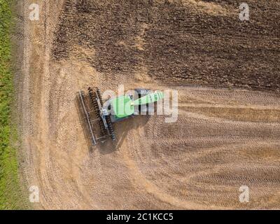 Top view of green tractor plowing the ground after harvesting on the field in the autumn time. Top view. Stock Photo