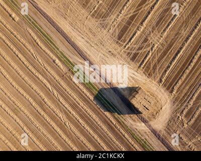 Top view from flying drones to an agricultural field after harvesting with a stacks of straw on it at summer day. Stock Photo