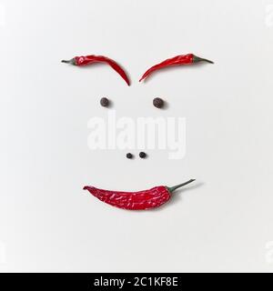 Creative pattern from red ripe chili pepper and pepper seeds in the form of mans face isolated on white background. Stock Photo