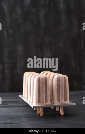 Frozen coffee drink on a stick in plastic form on a black wooden background with space for text. Cold flying dessert Stock Photo