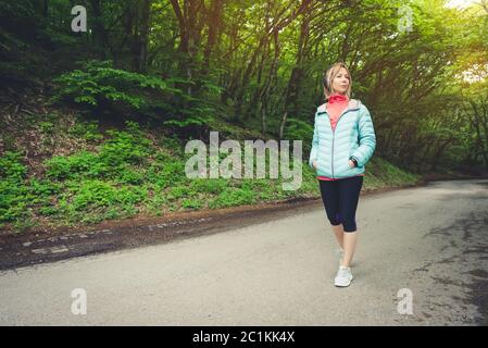 Portrait of an attractive sports girl blonde in a light running down jacket dressing bluetooth headphones with music or the soun Stock Photo