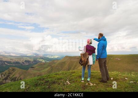 A young couple of tourists on the nature in the mountains point their hands towards the mountains. The concept of easy tourism Stock Photo