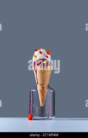 The waffle cone stands in glass jar with a ball of berry and vanilla ice cream with red and yellow pills and a lollipops on a da Stock Photo