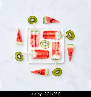 Creative pattern from different pieces of fruit and berry color ice cream on a stick in the shape of a square in a white plate o Stock Photo