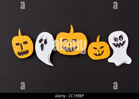 Colorful Halloween handcraft pattern with flying floating ghost spirit and smiling yellow pumpkins on a black paper background. Stock Photo