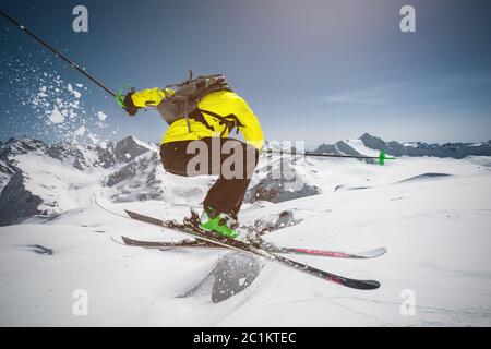 A skier in full sports equipment jumps into the abyss from the top of the glacier against the background of the blue sky and the Stock Photo