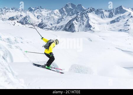 A skier in full sports equipment jumps into the precipice from the top of the glacier against the background of the blue sky and Stock Photo