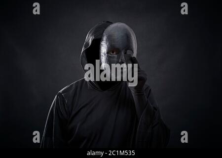 Scary figure in hooded cloak with mask in hand