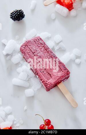 Berry black currant ice cream sorbet popsicles on crushed ice over a marble background with berries, top view Stock Photo