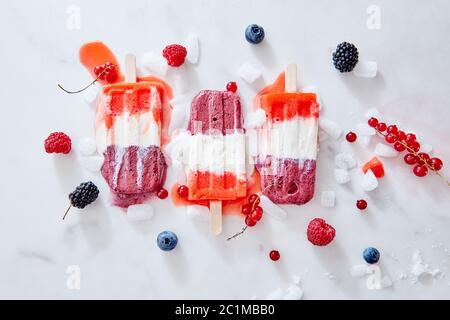 Tricolor strawberry and raspberry ice cream popsicles over ice with berries on marble background, top view and copy space Stock Photo