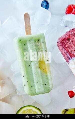 Homemade vegan frozen kiwi popsicles over the ice with slice lime, berries and kiwi, flat lay Stock Photo