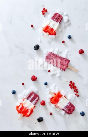 Tricolor homemade strawberry popsicles over ice with berries on marble background, top view Stock Photo